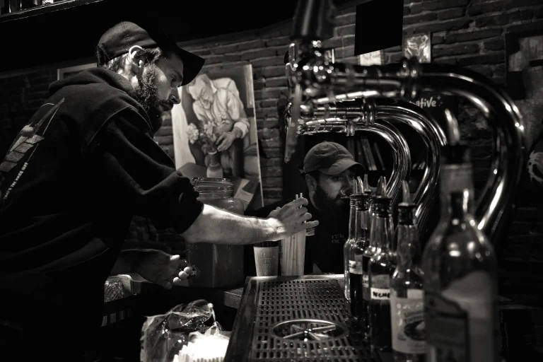 Programmation mars 2026 au Boudu Pont : concerts & soirées à Toulouse 3 Barman en train de préparer des boissons derrière le comptoir du Boudu Pont pendant une soirée animée.